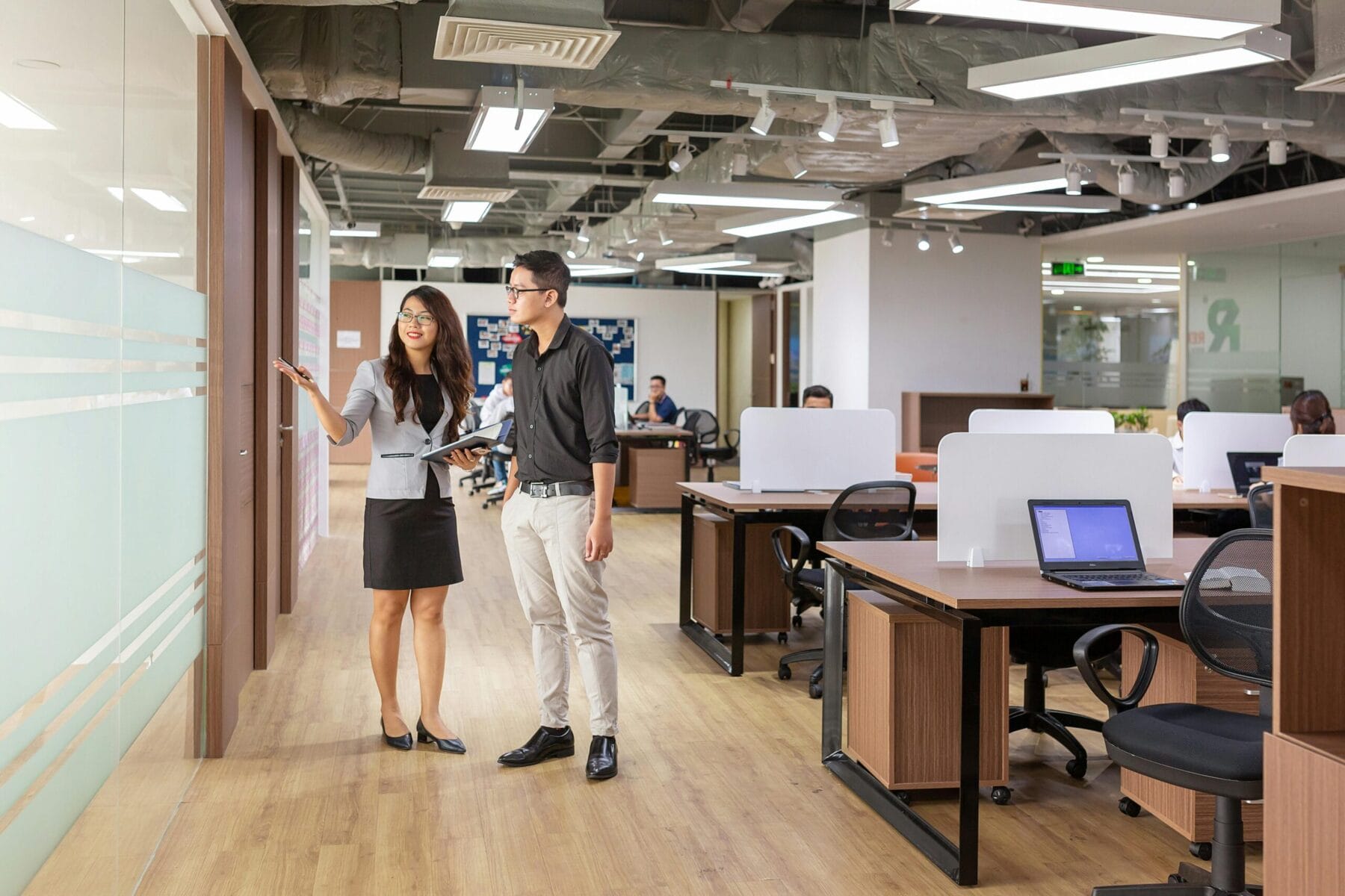 A busy modern office space featuring professionals actively collaborating in an open layout, working on laptops, engaging in discussions, and sharing ideas.