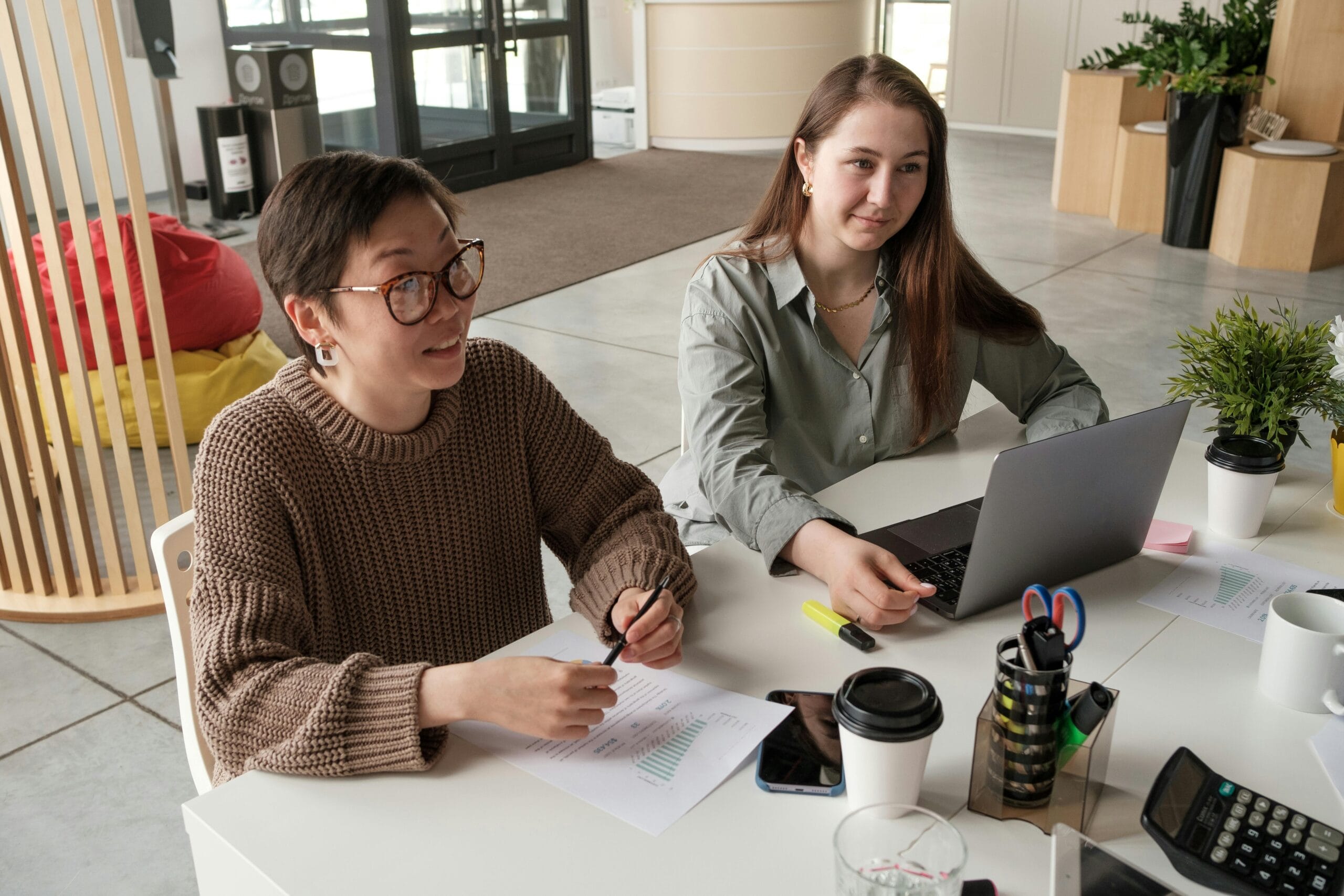 Two colleagues sitting at the same desk in an office, having a conversation and collaborating.