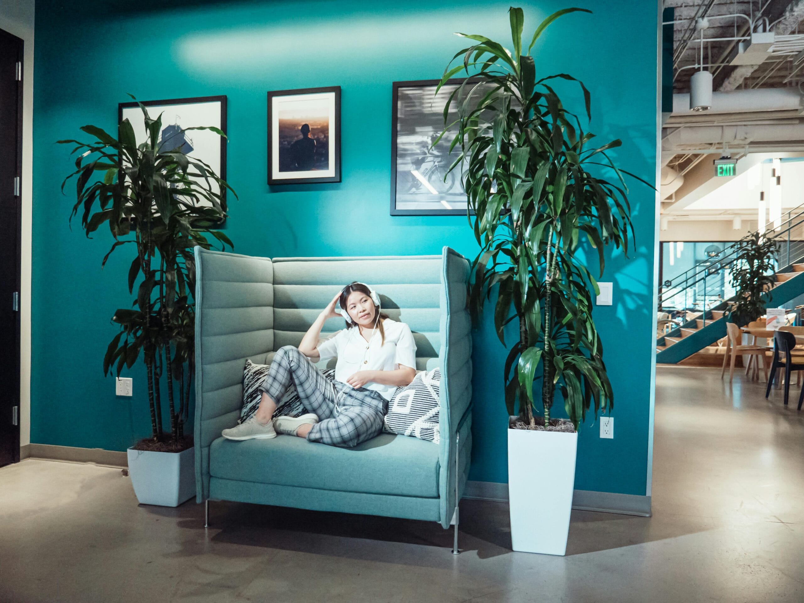 Woman relaxing in a modern office lounge with plants and vibrant turquoise wall