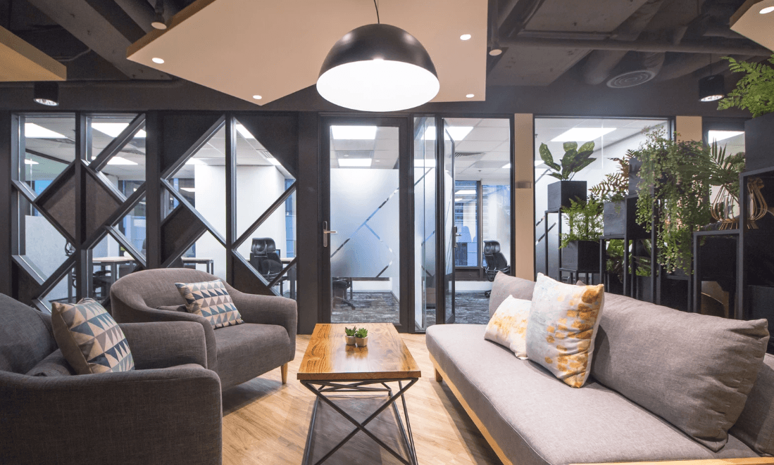 Modern office lounge with comfortable seating, wooden table, and plants.