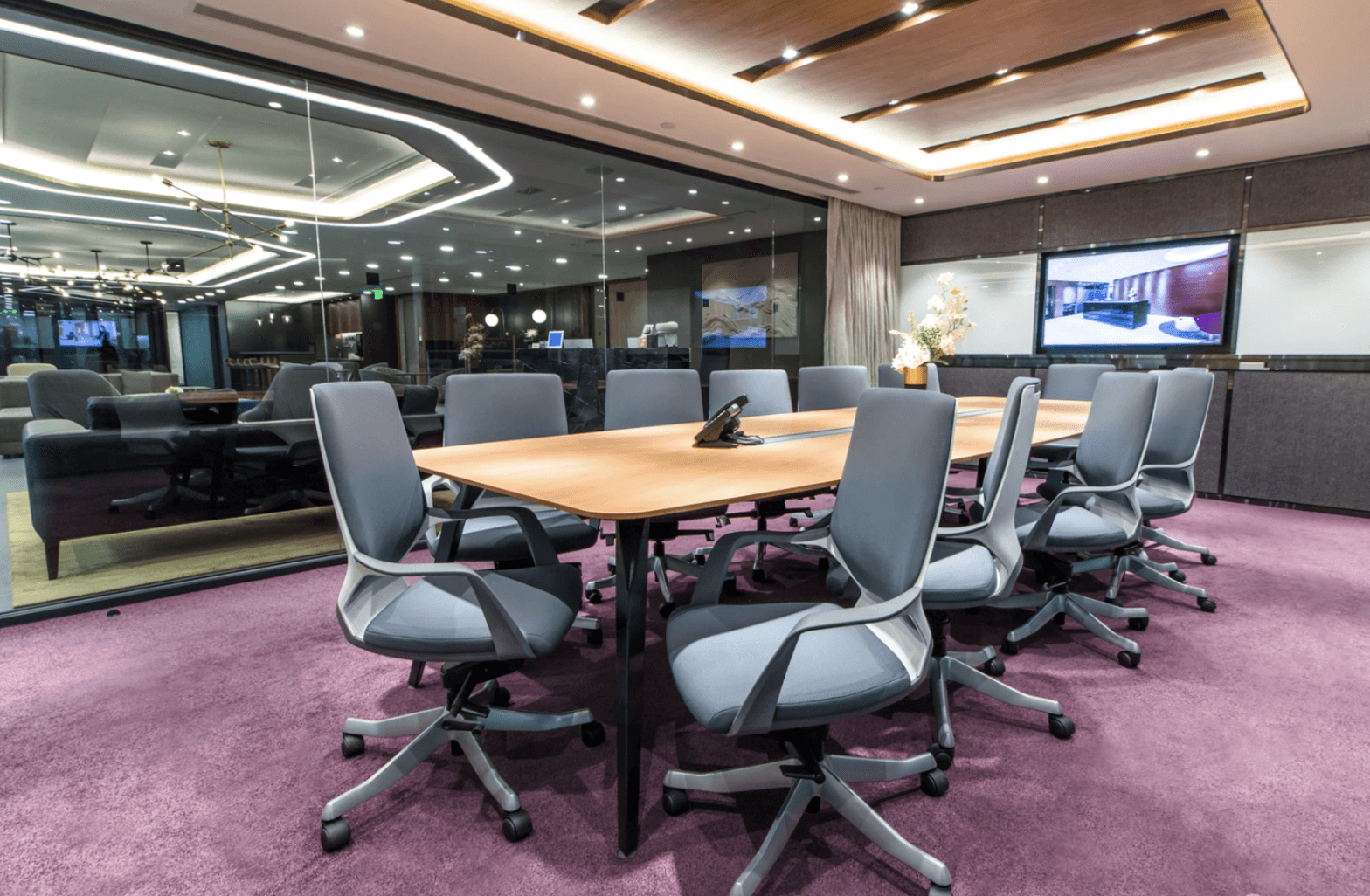 Modern boardroom with ergonomic chairs, large conference table, and built-in video screen display.