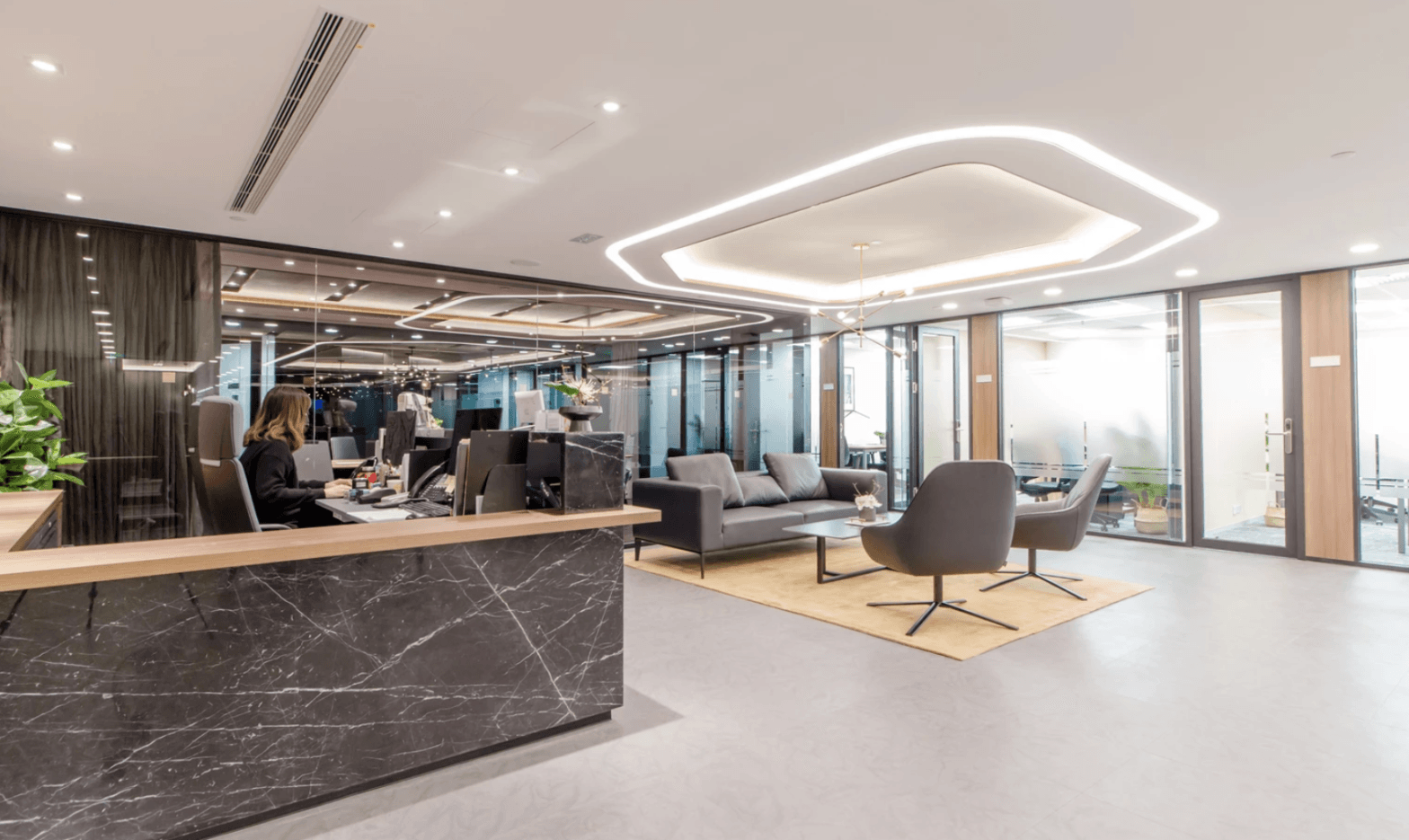 Luxurious office reception area with modern furniture, elegant lighting, and glass-walled meeting rooms.