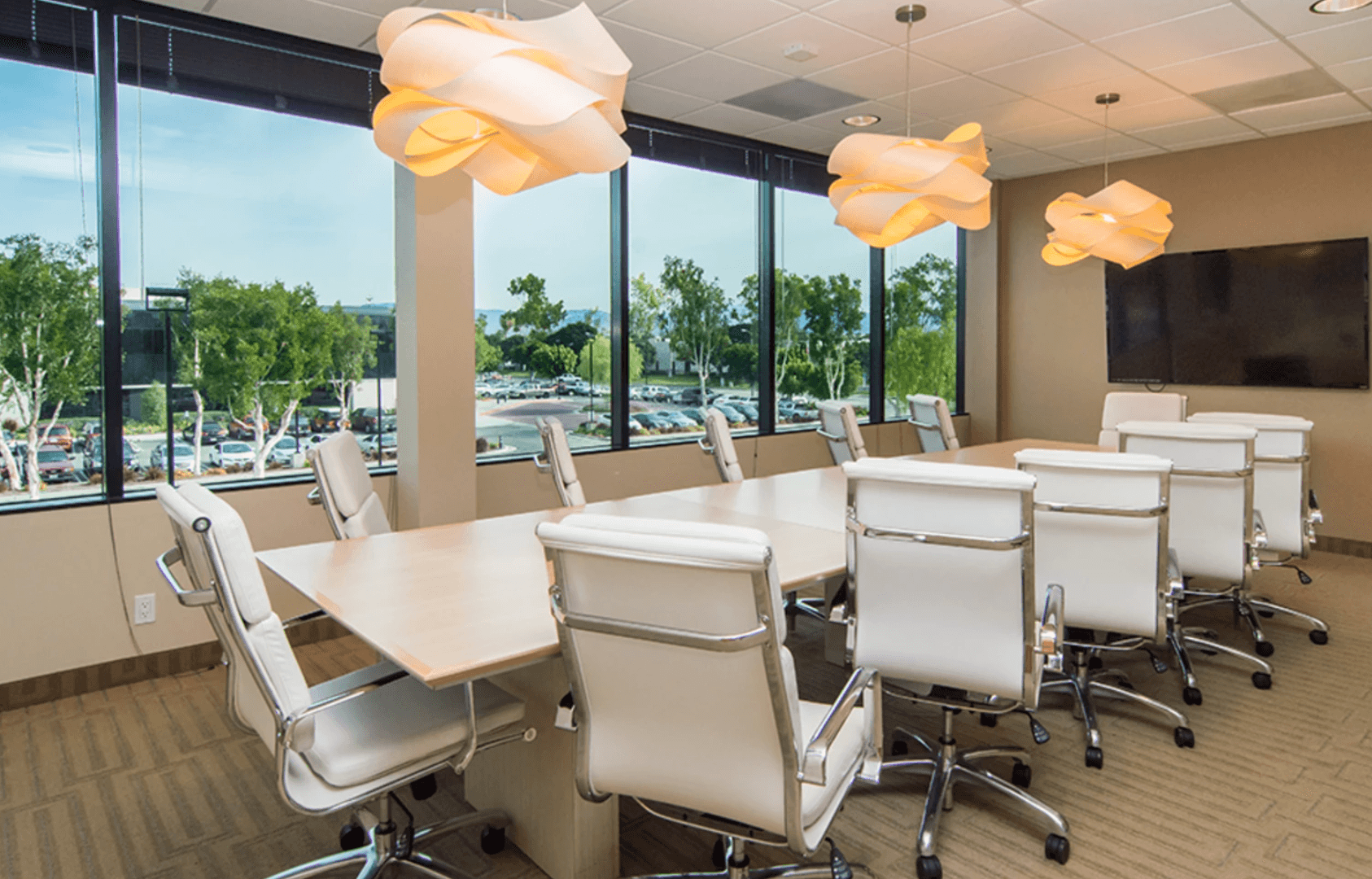 Bright conference room with white leather chairs, large table, modern lighting, and city views.